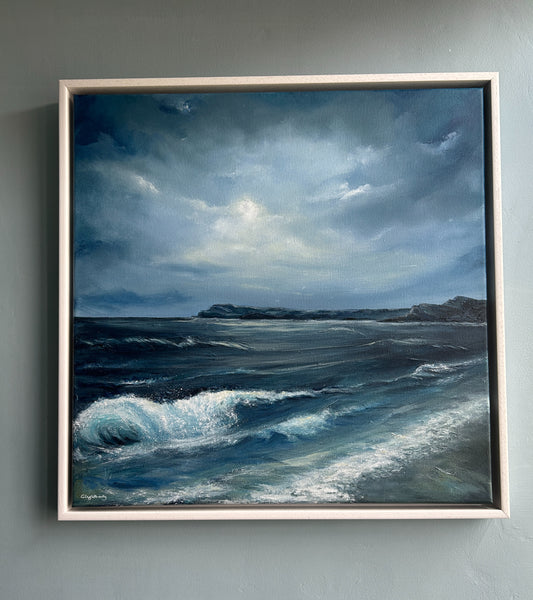 Framed painting of a stormy sea with a rocky island on a gray wall.