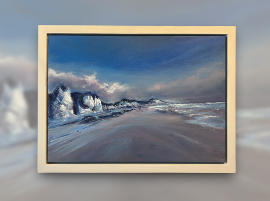 Framed artwork of a beach scene with waves and rocks on a wall.
